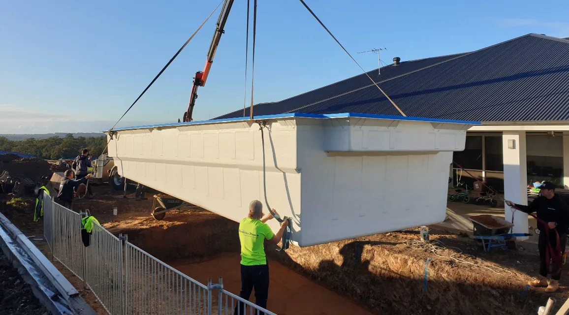 A crane is lifting a swimming pool into the ground.