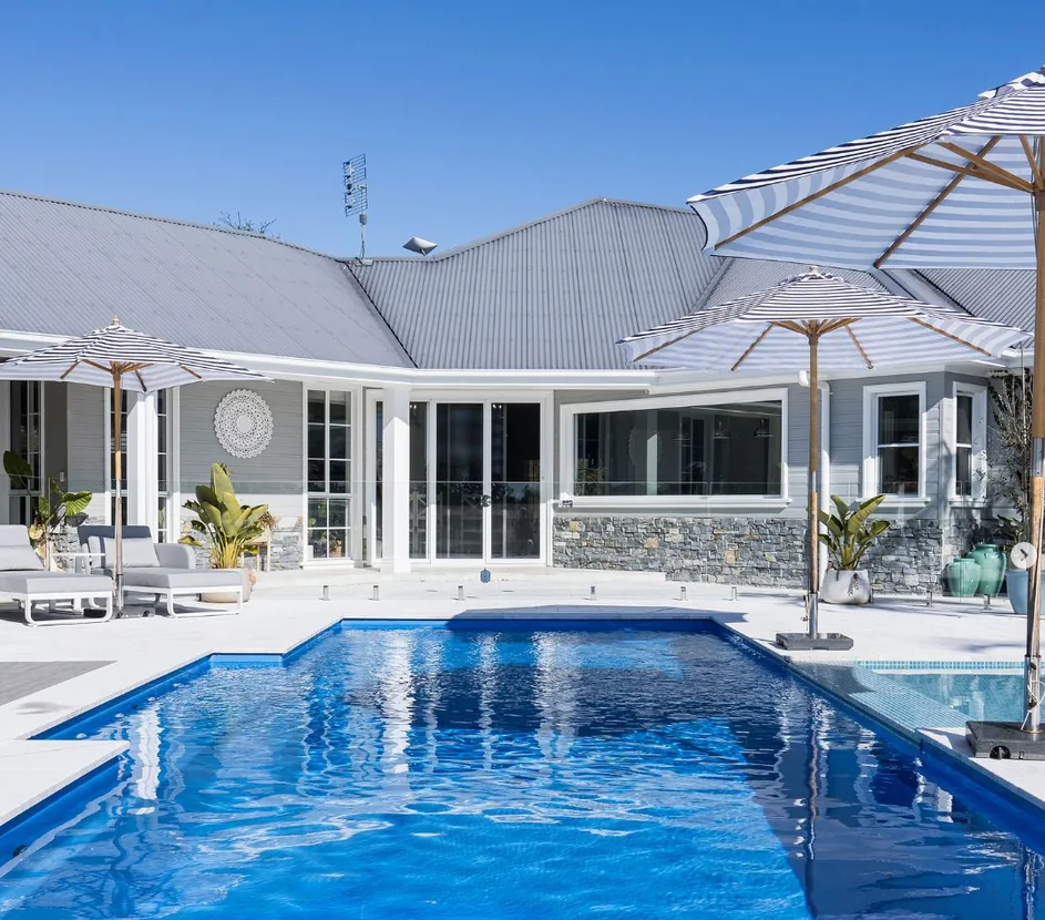 Large swimming pool by Masterbuilt Pools called 'The Heritage' in front of a house with umbrellas